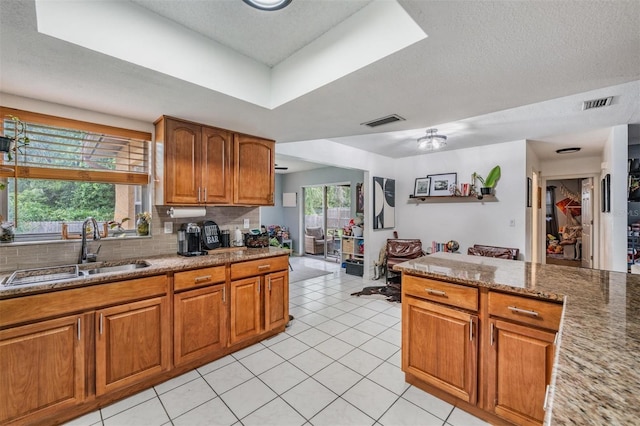 6101 Broken Arrow Dr, New Port Richey, FL 34653 - kitchen with brown cabinets, decorative backsplash, light tile patterned floors, light stone countertops, and a textured ceiling