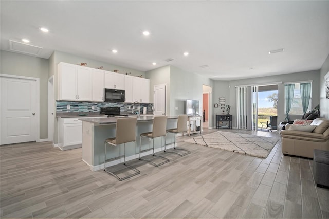 11829 Brighton Knoll Loop, Riverview, FL 33579 - kitchen with open floor plan, black appliances, light wood-type flooring, a center island with sink, and decorative backsplash