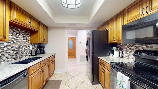 14424 Neptune Rd, Seminole, FL 33776 - kitchen with black appliances, brown cabinets, a tray ceiling, light tile patterned flooring, and light stone counters