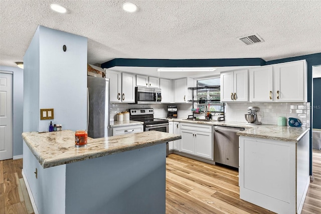 7814 Burnham Dr, Port Richey, FL 34668 - kitchen with appliances with stainless steel finishes, a peninsula, white cabinets, a textured ceiling, and backsplash