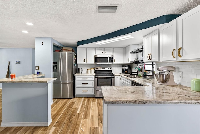 7814 Burnham Dr, Port Richey, FL 34668 - kitchen featuring appliances with stainless steel finishes, a peninsula, light wood-type flooring, a textured ceiling, and backsplash
