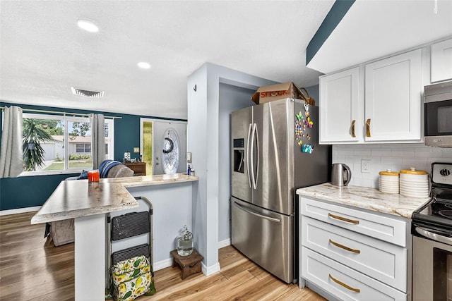 7814 Burnham Dr, Port Richey, FL 34668 - kitchen with appliances with stainless steel finishes, white cabinets, light wood finished floors, backsplash, and a kitchen breakfast bar
