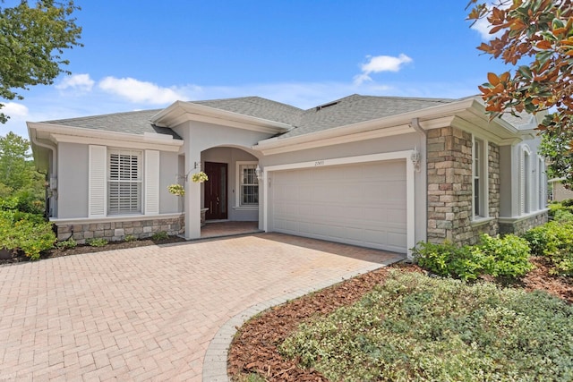 27455 Mistflower Dr, Wesley Chapel, FL 33544 - view of front of home featuring stone siding, an attached garage, a shingled roof, stucco siding, and decorative driveway