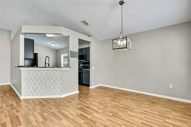 19635 Bellehurst Loop, Land O Lakes, FL 34638 - kitchen with range with gas cooktop, light wood finished floors, stainless steel microwave, vaulted ceiling, and a chandelier