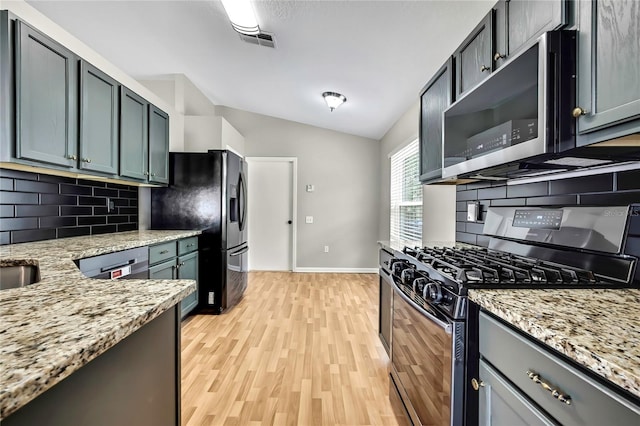 19635 Bellehurst Loop, Land O Lakes, FL 34638 - kitchen featuring appliances with stainless steel finishes, vaulted ceiling, tasteful backsplash, light wood finished floors, and light stone countertops