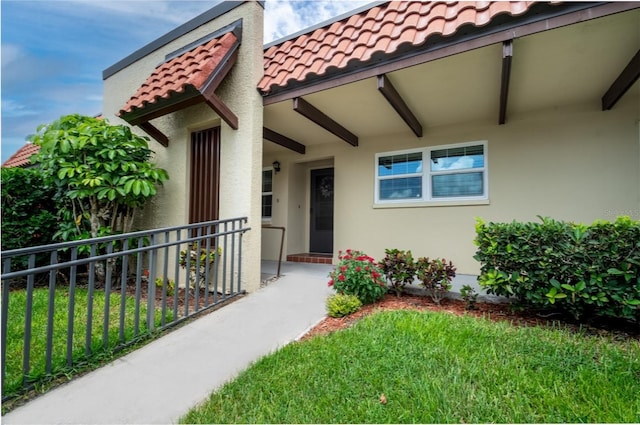 1701 Pinehurst Rd Unit 24B, Dunedin, FL 34698 - view of exterior entry with a tiled roof, stucco siding, and a lawn