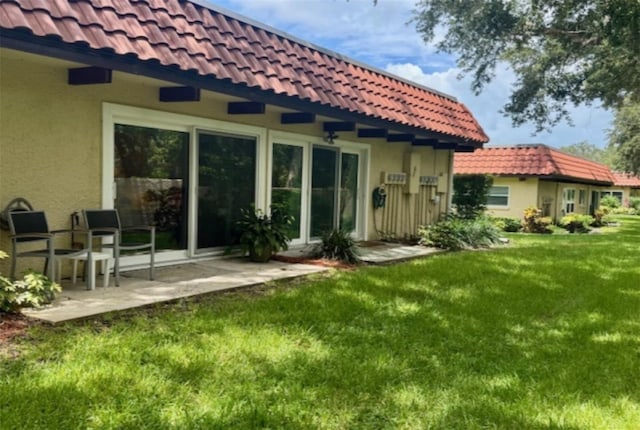 1701 Pinehurst Rd Unit 24B, Dunedin, FL 34698 - rear view of house featuring a tile roof, stucco siding, a lawn, and a patio area