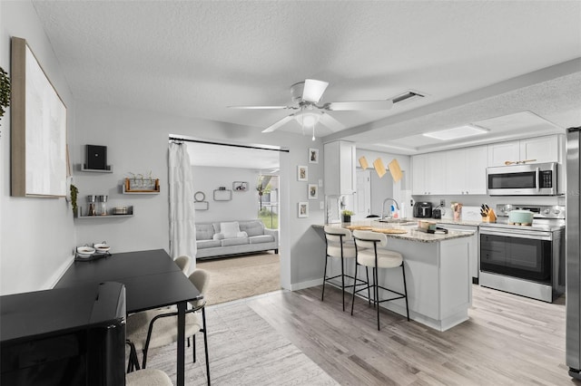 8004 Beaver Creek Loop, Hudson, FL 34667 - kitchen featuring stainless steel appliances, a kitchen bar, a textured ceiling, white cabinetry, and light wood-type flooring