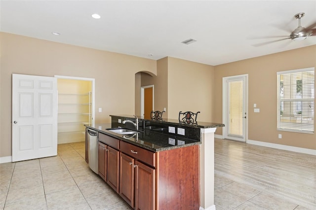 221 Sunset Crest Ct, Apollo Beach, FL 33572 - kitchen featuring arched walkways, light tile patterned floors, a ceiling fan, an island with sink, and dark stone counters