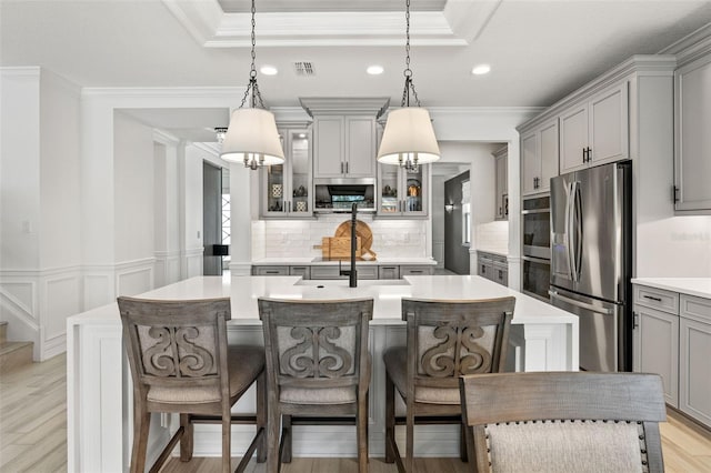 7819 Notched Pine Bnd, Wesley Chapel, FL 33545 - kitchen with appliances with stainless steel finishes, gray cabinetry, backsplash, a kitchen island with sink, and crown molding