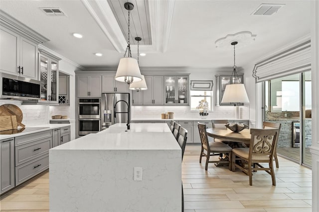 7819 Notched Pine Bnd, Wesley Chapel, FL 33545 - kitchen with gray cabinets, stainless steel appliances, crown molding, tasteful backsplash, and an island with sink
