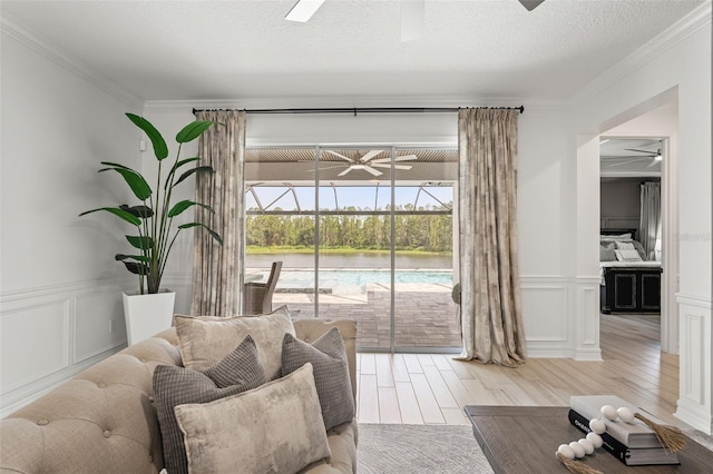 7819 Notched Pine Bnd, Wesley Chapel, FL 33545 - living area with a ceiling fan, light wood finished floors, a decorative wall, crown molding, and a wainscoted wall