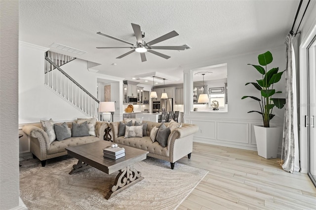 7819 Notched Pine Bnd, Wesley Chapel, FL 33545 - living area with ceiling fan, stairs, light wood-style floors, a textured ceiling, and a wainscoted wall