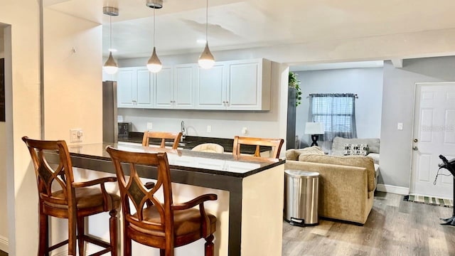 2813 W Kenmore Ave, Tampa, FL 33614 - kitchen featuring a kitchen breakfast bar, light wood-style floors, decorative light fixtures, dark countertops, and a peninsula