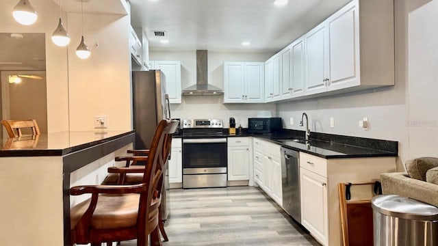 2813 W Kenmore Ave, Tampa, FL 33614 - kitchen with wall chimney exhaust hood, stainless steel appliances, light wood finished floors, a breakfast bar, and white cabinets
