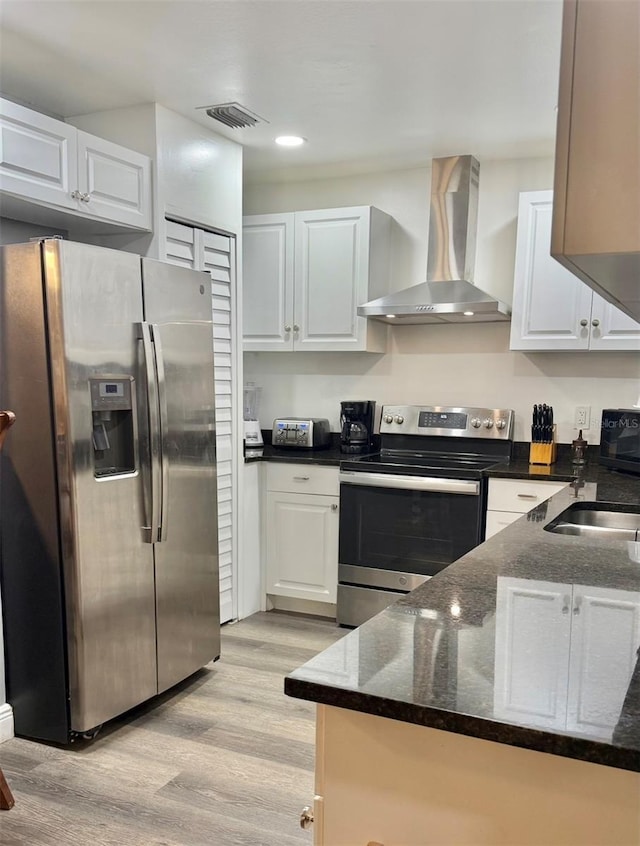 2813 W Kenmore Ave, Tampa, FL 33614 - kitchen featuring stainless steel appliances, wall chimney range hood, light wood-style floors, dark stone counters, and white cabinets