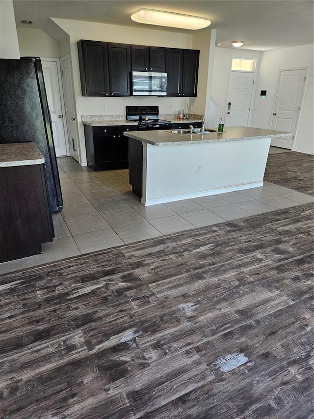 10124 Mangrove Well Rd, Ruskin, FL 33573 - kitchen with stainless steel microwave, electric stove, dark cabinetry, freestanding refrigerator, and wood finished floors