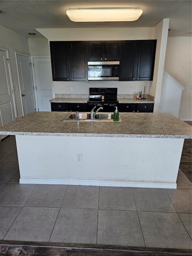 10124 Mangrove Well Rd, Ruskin, FL 33573 - kitchen with stainless steel microwave, black range with electric cooktop, dark cabinets, and a center island with sink