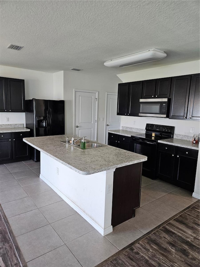10124 Mangrove Well Rd, Ruskin, FL 33573 - kitchen featuring black appliances, dark cabinetry, a center island with sink, light countertops, and a textured ceiling