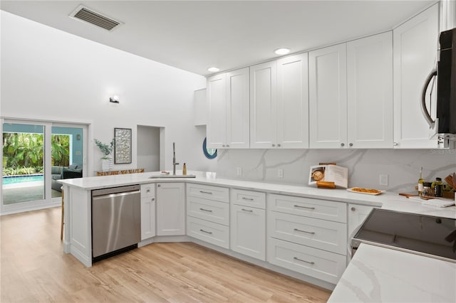 221 42nd Ave, St Pete Beach, FL 33706 - kitchen with appliances with stainless steel finishes, a peninsula, white cabinetry, light wood finished floors, and recessed lighting