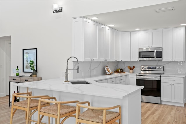 221 42nd Ave, St Pete Beach, FL 33706 - kitchen with stainless steel appliances, a peninsula, light wood finished floors, light stone countertops, and recessed lighting