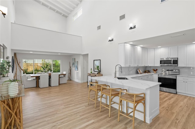 221 42nd Ave, St Pete Beach, FL 33706 - kitchen featuring appliances with stainless steel finishes, a high ceiling, a breakfast bar area, light stone countertops, and a peninsula