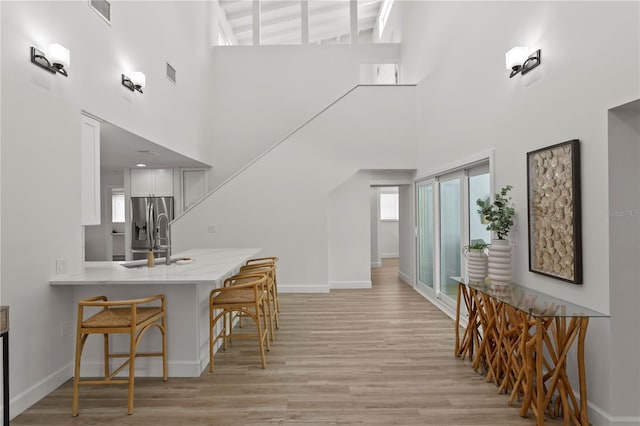 221 42nd Ave, St Pete Beach, FL 33706 - kitchen featuring a towering ceiling, a kitchen breakfast bar, light wood-style floors, white cabinets, and stainless steel refrigerator with ice dispenser