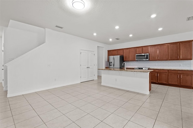 12124 Lake Blvd, Trinity, FL 34655 - kitchen with appliances with stainless steel finishes, an island with sink, decorative backsplash, light stone counters, and brown cabinetry