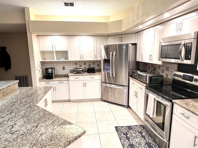 1304 N Jasmine Ave, Tarpon Springs, FL 34689 - kitchen featuring appliances with stainless steel finishes, open shelves, decorative backsplash, a textured ceiling, and light tile patterned flooring