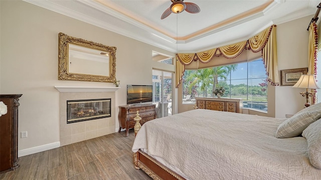15110 Sundial Pl, Lakewood Ranch, FL 34202 - bedroom featuring crown molding, wood finished floors, a tiled fireplace, a tray ceiling, and ceiling fan