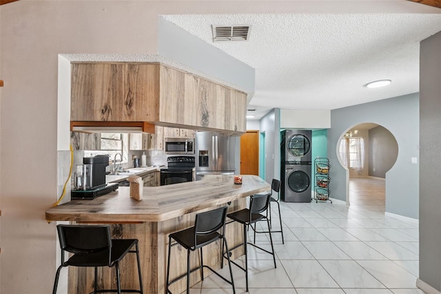 1116 Dagmar Ave, Spring Hill, FL 34606 - kitchen featuring appliances with stainless steel finishes, stacked washer / dryer, arched walkways, a breakfast bar, and a peninsula