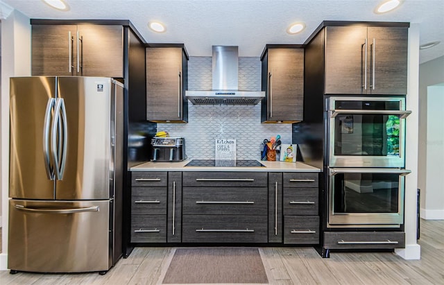 1120 Lancer Ln, Tarpon Springs, FL 34689 - kitchen with stainless steel appliances, wall chimney exhaust hood, tasteful backsplash, light wood-style floors, and light countertops