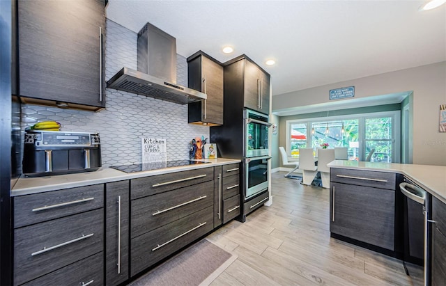 1120 Lancer Ln, Tarpon Springs, FL 34689 - kitchen featuring wall chimney range hood, appliances with stainless steel finishes, decorative backsplash, light countertops, and light wood finished floors