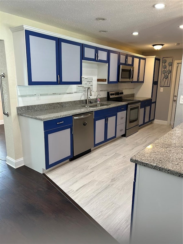 3260 Parkway Pl, Palm Harbor, FL 34684 - kitchen with stainless steel appliances, blue cabinets, light wood-style floors, backsplash, and recessed lighting