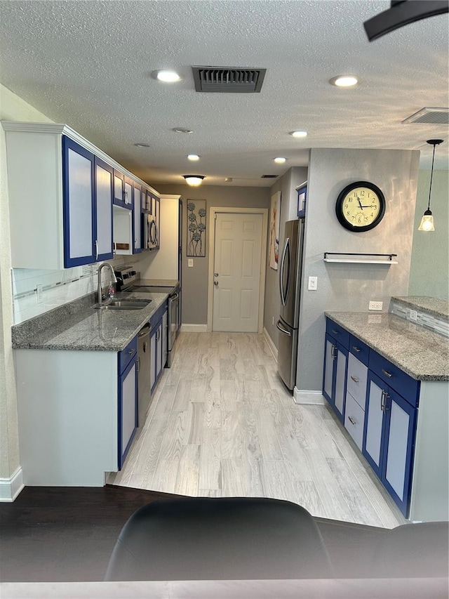 3260 Parkway Pl, Palm Harbor, FL 34684 - kitchen with blue cabinetry, appliances with stainless steel finishes, light wood finished floors, a textured ceiling, and stone counters