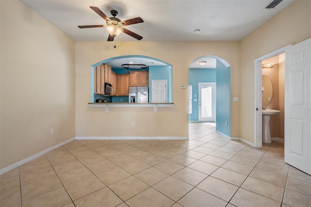 14167 Stilton St, Tampa, FL 33626 - kitchen featuring stainless steel appliances, a ceiling fan, light tile patterned flooring, arched walkways, and brown cabinetry