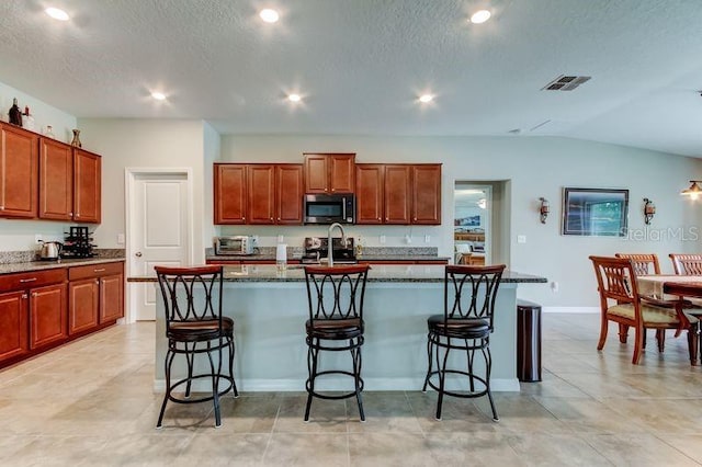 6395 Cobble Bliss St, Zephyrhills, FL 33541 - kitchen with stainless steel microwave, a breakfast bar area, black electric range oven, a center island with sink, and recessed lighting