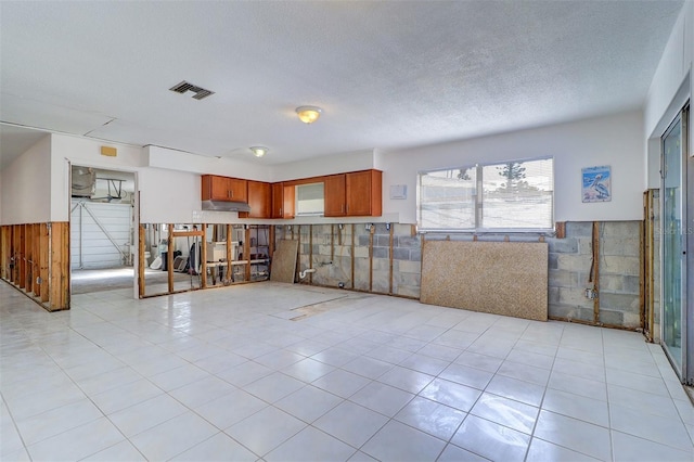 123 11th Ave, Indian Rocks Beach, FL 33785 - kitchen with a wainscoted wall, a textured ceiling, brown cabinetry, light tile patterned flooring, and under cabinet range hood