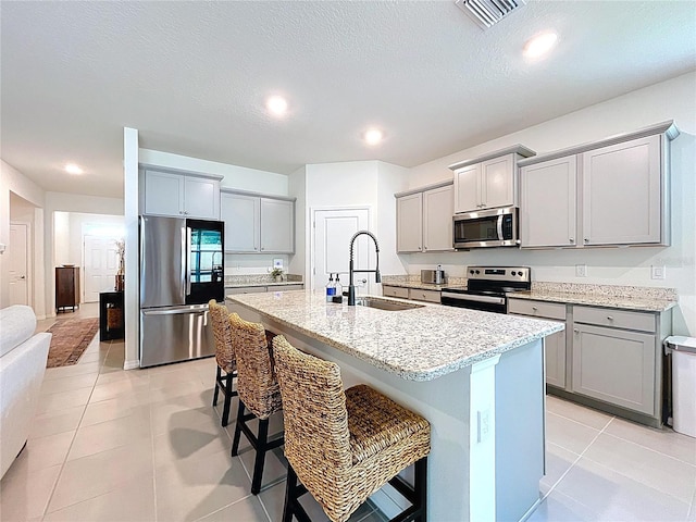 8214 Wheat Stone Dr, Zephyrhills, FL 33540 - kitchen featuring stainless steel appliances, gray cabinetry, a center island with sink, a breakfast bar, and recessed lighting