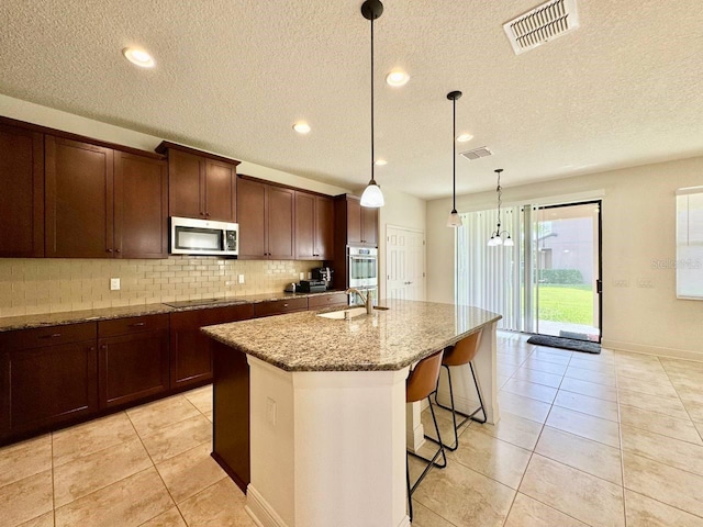 19502 Sea Myrtle Way, Tampa, FL 33647 - kitchen with stainless steel appliances, decorative backsplash, light stone counters, light tile patterned flooring, and an island with sink