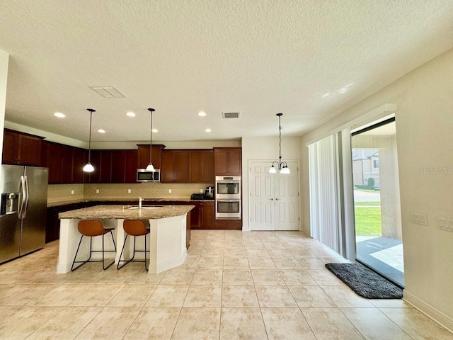 19502 Sea Myrtle Way, Tampa, FL 33647 - kitchen featuring appliances with stainless steel finishes, tasteful backsplash, light stone counters, a kitchen island with sink, and pendant lighting