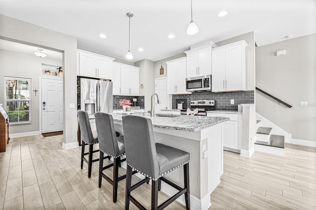 9237 Fox Sparrow Rd, Tampa, FL 33626 - kitchen featuring appliances with stainless steel finishes, light wood finished floors, a kitchen breakfast bar, hanging light fixtures, and a kitchen island with sink