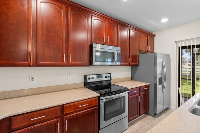 30151 Goodwick Way, Wesley Chapel, FL 33543 - kitchen with appliances with stainless steel finishes, reddish brown cabinets, light tile patterned flooring, light stone counters, and recessed lighting
