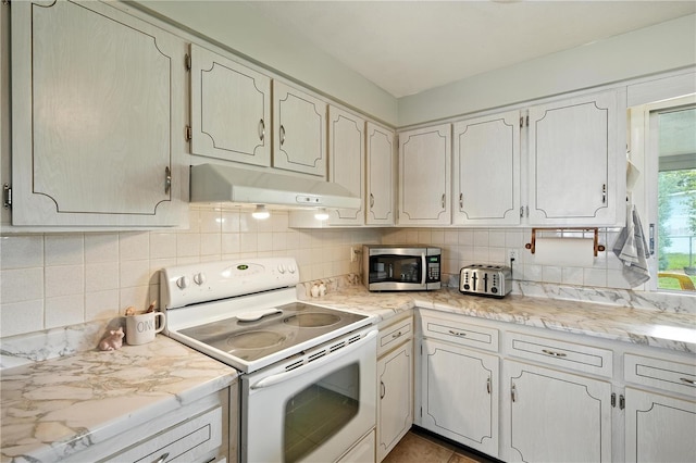5628 Cypress St, Zephyrhills, FL 33542 - kitchen with electric range, under cabinet range hood, stainless steel microwave, light countertops, and decorative backsplash