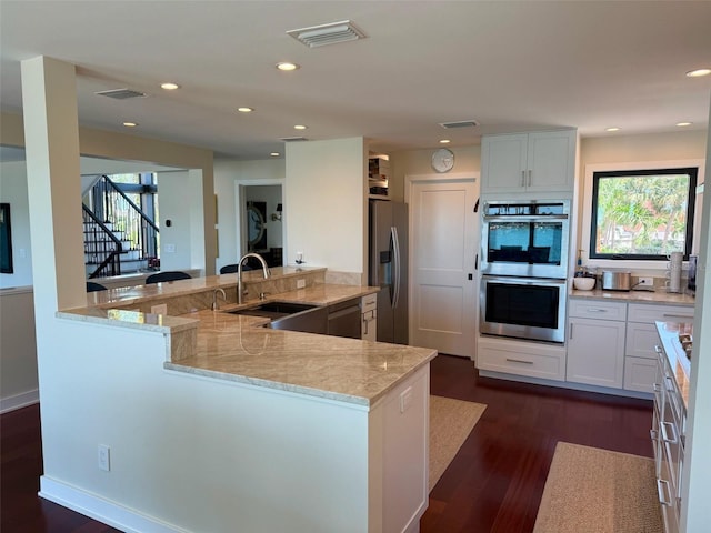 850 59th Ave, Saint Petersburg, FL 33706 - kitchen featuring stainless steel appliances, dark wood-style flooring, light stone countertops, white cabinetry, and a peninsula