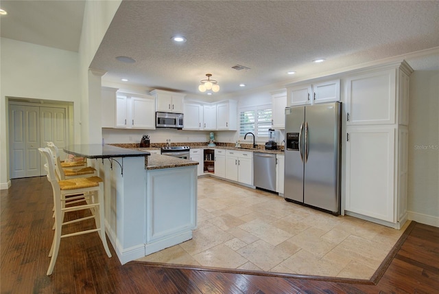 14 Evonaire Cir, Belleair, FL 33756 - kitchen featuring stainless steel appliances, a peninsula, white cabinets, a textured ceiling, and dark stone countertops