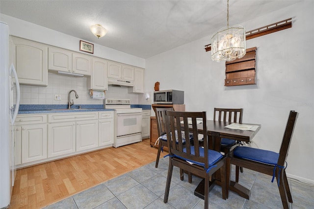 4357 Tahitian Gardens Cir Unit B, Holiday, FL 34691 - kitchen featuring white appliances, a chandelier, under cabinet range hood, decorative backsplash, and light wood finished floors