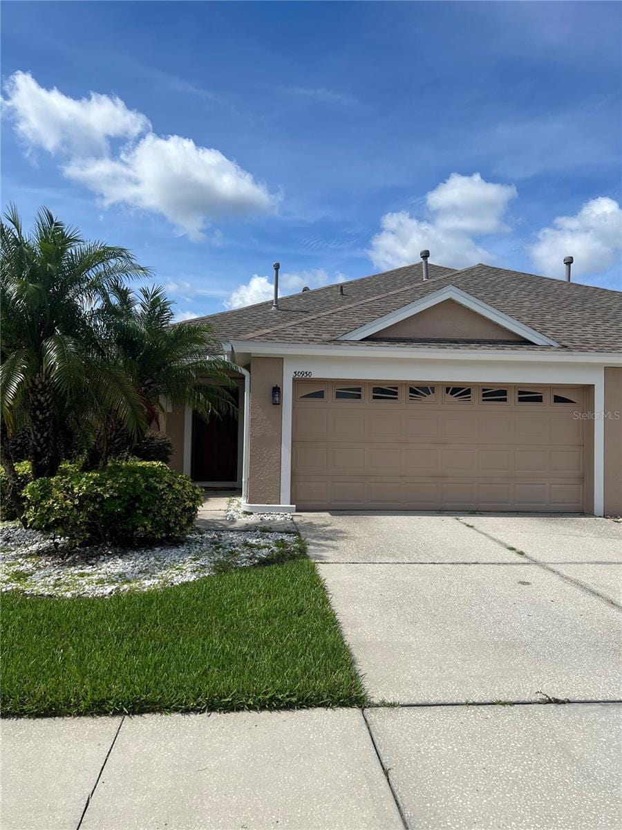 30930 Whitlock Dr, Wesley Chapel, FL 33543 - ranch-style house featuring an attached garage, stucco siding, concrete driveway, and roof with shingles