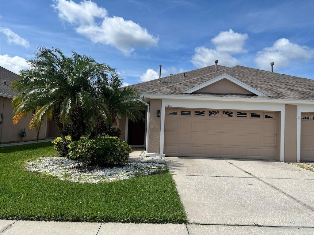 30930 Whitlock Dr, Wesley Chapel, FL 33543 - ranch-style home with a garage, concrete driveway, stucco siding, a shingled roof, and a front lawn