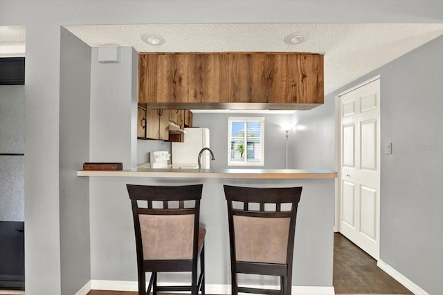 250 Cypress Ln, Oldsmar, FL 34677 - kitchen with freestanding refrigerator, a textured ceiling, a peninsula, a breakfast bar area, and light countertops